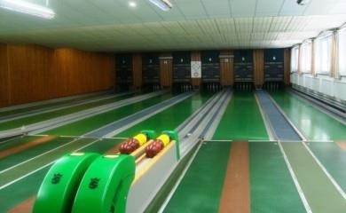 Eine Bowlingbahn mit mehreren Bahnen und bunten Kegelkasten. Der Raum hat große Fenster und eine helle Atmosphäre.