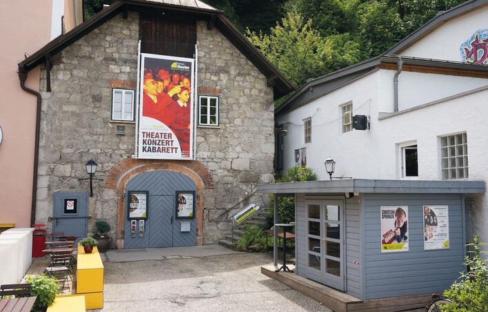 Ein charmantes Theatergebäude mit einer großen Plakatwand, das kulturelle Veranstaltungen anbietet. Nebenan befindet sich ein kleiner Kiosk mit bunten Anzeigen.