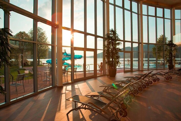 Ein heller Innenraum mit großen Fenstern, die den Blick auf einen Pool und die Natur ermöglichen. Die Sonne scheint durch die Fenster und schafft eine entspannende Atmosphäre.