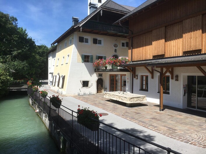 Ein charmantes Gebäude am Wasser mit Blumenkästen und einer einladenden Terrasse. Der ruhige Fluss nebenan verleiht der Szene eine idyllische Atmosphäre.