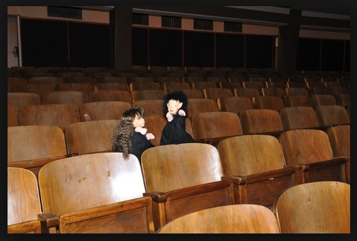 Kino Attnang-Puchheim in Attnang-Puchheim: In dem Bild sieht man zwei Personen, die allein in einem großen leeren Theatersaal sitzen. Der Raum hat Holzbänke und ist sehr dunkel, bis auf einige Lampen an der Decke. Die beiden Personen sitzen in der Mitte des Saals und scheinen in einer ruhigen und nachdenklichen Stimmung zu sein.