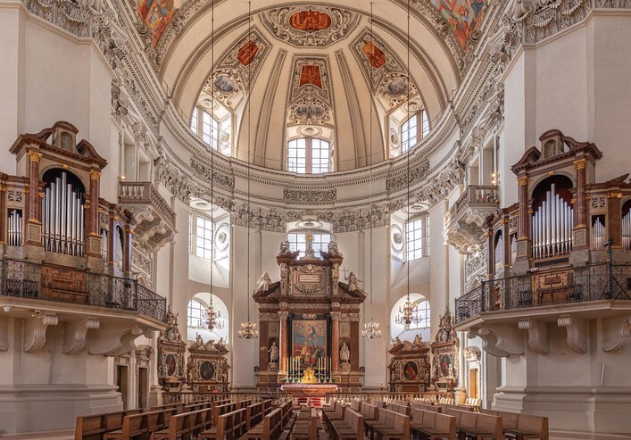 Eine prächtige Kirche mit einer hohen Kuppel und kunstvollen Deckenfresken. Bänke und Orgeln flankieren den Altar in der Mitte.