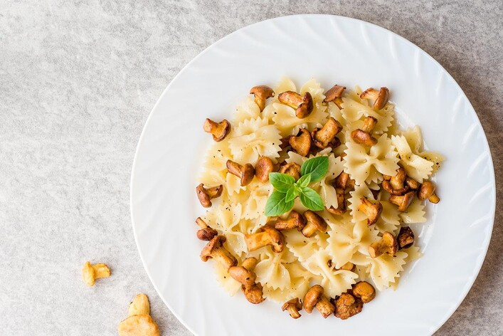 Ein Teller Pasta mit Pilzen und frischem Basilikum. Die Farfalle sind lecker angerichtet und laden zum Essen ein.