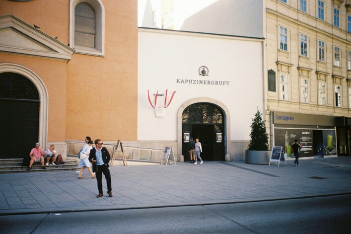 People outside a building with arched entrance and signage.
