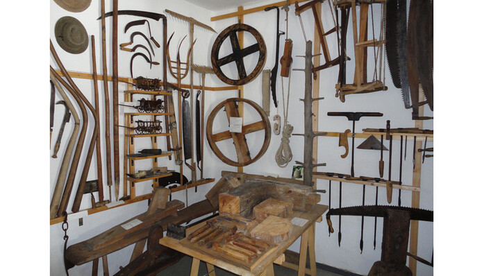 Heimathaus Schörfling in Schörfling am Attersee: Das Bild zeigt eine Werkstatt voller historischer Werkzeuge und Geräte. An den Wänden hängen zahlreiche Holzräder, Haken und andere traditionelle Gerätschaften, die auf eine handwerkliche Tradition hinweisen.