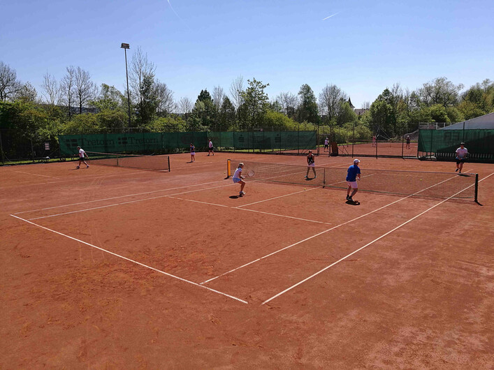 ATSV Schärding Tennis in Schärding: Eine Tennisanlage mit mehreren Tennisplätzen, auf denen Spieler aktiv sind. Die Plätze haben eine rötliche Lehmbahn-Oberfläche und sind von grünen Zäunen umgeben. In der Umgebung befinden sich Bäume und weitere Gebäude.