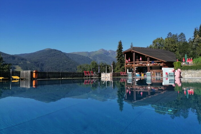 Ein schöner Pool mit glattem Wasser und einer gemütlichen Terrasse. Im Hintergrund sind Berge und ein klarer blauer Himmel zu sehen.