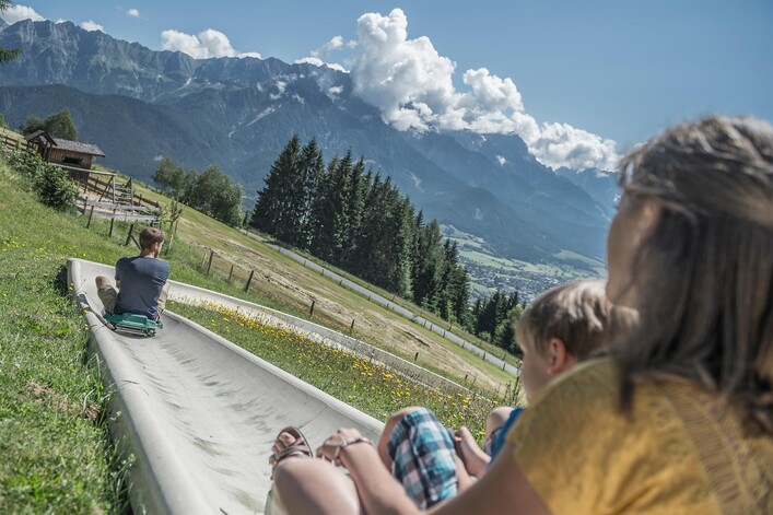 Ein Rutschenabenteuer inmitten einer schönen Berglandschaft. Im Hintergrund erheben sich majestätische Berge unter einem klaren Himmel.