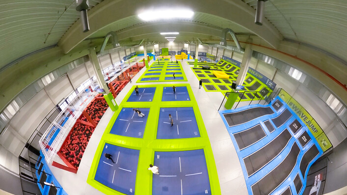 Jump Dome Linz in Leonding: Eine große und moderne Sporthalle mit verschiedenen Trainingsgeräten und Trampolinen. Bunte Farben und eine offene Raumaufteilung prägen den Eindruck. Die Halle scheint für unterschiedliche Sportarten und Aktivitäten ausgelegt zu sein.