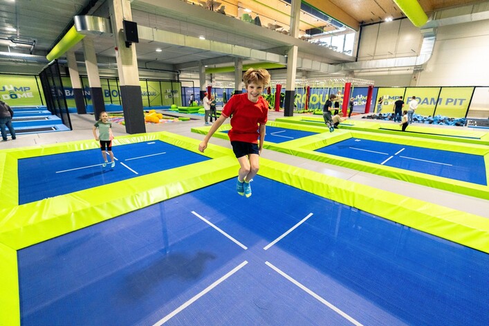 Ein Trampolinpark mit bunten Trampolinen in hellgrüner und blauer Farbe. Mehrere Jugendliche hüpfen und haben Spaß in der Einrichtung.