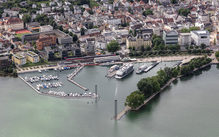 Luftbild vom Hafen Bregenz bei sehr hohem Wasserstand. Links und rechts der Hafeneinfahrt stehen die beiden Leuchttürme. Auf der linken Seite sieht man den Yachthafen (Marina Bregenz), in der Mitte das Hafengelände, das ausschließlich für die Kursschifffahrt bestimmt ist und rechts das Blumenmolo.