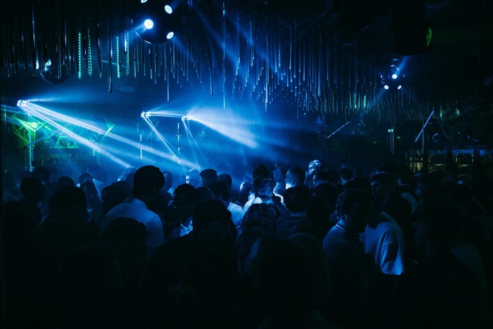 Eine lebhafte Partyszene mit vielen Menschen. Stimmungsvolle Lichter in blauen und grünen Tönen schaffen eine aufregende Atmosphäre.