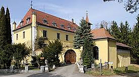 Schloss Au in Roitham am Traunfall: Das Bild zeigt ein historisches Gebäude mit traditionellen Architekturstilen. Es ist von Bäumen und Vegetation umgeben und hat einen Torbogen als Haupteingang. Das Gebäude ist mehrstöckig und hat ein Dach mit roten Ziegeln.