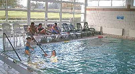 Hallenbad Haibach in Haibach ob der Donau: Eine Gruppe von Menschen in einem Schwimmbeckenbereich. Es sieht nach einer Anlage aus, mit Sitzgelegenheiten am Rand und großen Fenstern, die einen Blick nach draußen auf eine Landschaft ermöglichen. Die Personen befinden sich teilweise im Wasser, während andere darauf warten, hineinzugehen oder am Rand stehen.