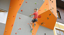 Ein Mann klettert an einer bunten Kletterwand. Die Wand hat viele Griffe in verschiedenen Farben.