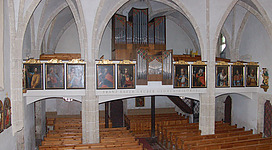 Franz Xaver Gruber Gedächtnisorgel in Hochburg-Ach: Eine Kirche mit hohen Gewölbebögen, im Inneren mit Altarbildern an den Wänden und einer imposanten Orgel in der Mitte. Mehrere Holzbänke sind für Besucher arrangiert.
