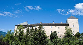 Eine beeindruckende Burg umgeben von grünen Bäumen. Der Himmel ist klar und blau.