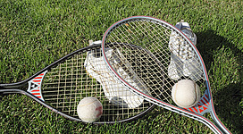 Tennis Schiemer in Weyregg am Attersee: Das Bild zeigt zwei Tennisschläger und zwei Tennisbälle auf einer grünen Rasenfläche. Die Tennisschläger sind in einem klassischen Design gehalten und vermitteln den Eindruck eines sportlichen Hobbys oder einer Freizeit-Aktivität.