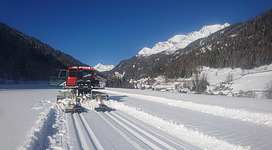 Ein Schneepflug auf einer verschneiten Fläche mit Bergen im Hintergrund. Der klare blaue Himmel sorgt für eine schöne Winteratmosphäre.