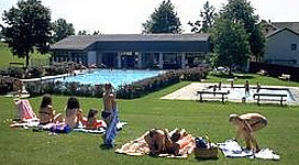 Beach-Volleyballplatz in Hofkirchen im Mühlkreis: Ein mehrstöckiges Gebäude mit traditioneller Architektur, umgeben von Grünflächen und Bäumen. Menschen sitzen und liegen auf Picknicktischen und Liegestühlen auf der Rasenfläche davor.