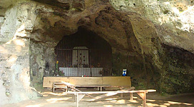Eine Höhle mit einem einfachen Altar und Holzbank. Die Wände sind rau und unregelmäßig geformt.