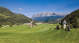 Ein malerischer Golfplatz inmitten der Berge mit grünem Rasen. Zwei Spieler genießen die herrliche Aussicht auf die Landschaft.