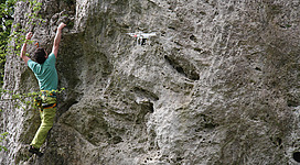 Ein Kletterer greift an einer Felswand, während eine Drohne in der Nähe fliegt. Die Szene zeigt Abenteuer und moderne Technologie im Freien.