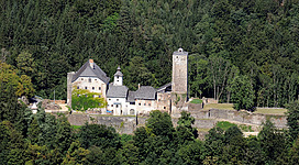Schloss Marsbach in Hofkirchen im Mühlkreis: Ein charmantes historisches Gebäude thront auf einer Anhöhe, umgeben von dichtem, grünem Wald. Der stattliche Turm ragt aus der Fassade hervor und verleiht dem Anwesen einen markanten Charakter. Die Fassade ist hell verputzt und zeigt traditionelle Architekturelemente, die auf eine lange Geschichte hinweisen.