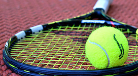 Ein Tennisschläger liegt auf dem Boden neben einem gelben Tennisball. Der Schläger hat ein auffälliges Design mit grünen Akzenten.