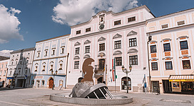 Museum Lauriacum in Enns: Ein großes, mehrstöckiges Gebäude mit einer beeindruckenden Fassade. Die Architektur ist im traditionellen Stil mit vielen Verzierungen und Ornamenten gestaltet. Vor dem Gebäude befindet sich ein Brunnen mit einer Statue. Insgesamt vermittelt das Bild einen historischen, eleganten Eindruck.
