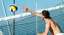 Beachvolleyballplatz in Lengau: Ein Volleyballspieler, der versucht, den Ball über das Netz zu spielen. Er hat seinen Arm erhoben, um den Ball zu schlagen. Im Hintergrund ist ein klarer blauer Himmel zu sehen.