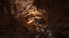 Eine beeindruckende Höhle mit schimmernden Felsen und einem Holzweg. Sanftes Licht beleuchtet die Stalaktiten und die beeindruckende Felsformation.