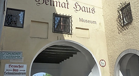 Heimatmuseum Obernberg am Inn in Obernberg am Inn: Auf dem Bild ist ein historisch anmutendes Museumsgebäude mit einem Torbogen zu sehen. Es trägt den Namen "Heimat Haus Museum" in deutscher Schrift. Das Gebäude hat ein traditionelles Aussehen mit Natursteinbogen und Fenstern. Außerdem ist ein Schild für Öffnungszeiten und Eintrittspreise zu erkennen.