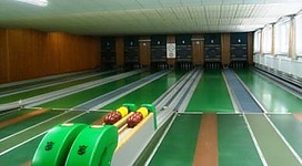 Eine Bowlingbahn mit mehreren Bahnen und bunten Kegelkasten. Der Raum hat große Fenster und eine helle Atmosphäre.