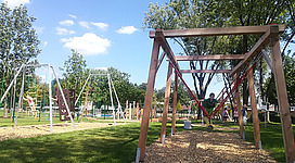 Motorikpark ® Andorf in Andorf: In dem Bild sieht man einen Spielplatz mit verschiedenen Klettergerüsten und Schaukeln. Die Anlage befindet sich in einer parkähnlichen Umgebung mit Bäumen und Grünflächen. Es herrscht eine sommerliche, entspannte Atmosphäre an diesem Ort.