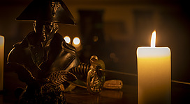 Napoleon "Premium-Escape Room", Linz: Bronzestatue eines Generals mit Dreispitz neben brennender Kerze in dunklem Raum.