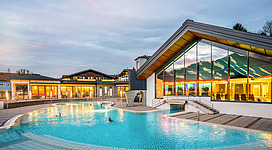 Ein modernes Schwimmbad mit klarblauem Wasser und einer einladenden Architektur. Im Hintergrund sind große Fenster, die einen Blick auf die Umgebung bieten.