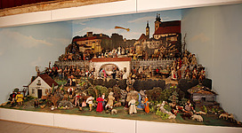 Eine große Krippe mit vielen Figuren, die verschiedene Szenen darstellen. Im Hintergrund sind Gebäude und eine Landschaft sichtbar.