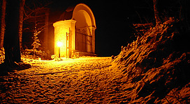 Beleuchteter Pilgerweg über den Falkenstein in St. Wolfgang im Salzkammergut: Das Bild zeigt ein leuchtend erleuchtetes Gebäude in einer winterlichen Landschaft. Der Weg ist mit Schnee bedeckt, was eine friedliche und stimmungsvolle Atmosphäre schafft.