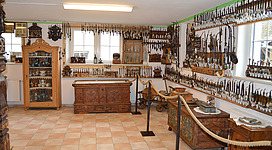 Museum „Historische Sammlung“ in Höhnhart: In diesem Bild ist ein Innenraum zu sehen, der offensichtlich ein Museum oder ein Geschäft für traditionelle Werkzeuge und Geräte darstellt. Die Wände sind mit einer großen Auswahl an verschiedenen Werkzeugen und Gegenständen dekoriert, darunter Hämmer, Sensen, Sicheln und andere landwirtschaftliche Geräte. In der Mitte des Raums befindet sich eine Theke oder ein Tresen, an dem verschiedene Waren ausgestellt sind. Insgesamt vermittelt der Raum einen Eindruck von Tradition und handwerklicher Arbeit.