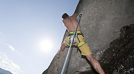 Ein climber erklimmt eine steile Felswand unter einem klaren Himmel. Die Sonne strahlt im Hintergrund.