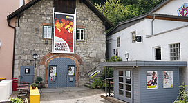 Ein charmantes Theatergebäude mit einer großen Plakatwand, das kulturelle Veranstaltungen anbietet. Nebenan befindet sich ein kleiner Kiosk mit bunten Anzeigen.