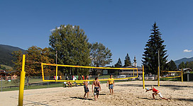 Freunde spielen Beachvolleyball auf dem Sandplatz bei blauem Himmel und Sonnenschein.