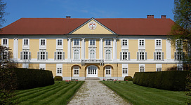 Fürstlich Starhemberg'sches Familien- und Stadtmuseum in Eferding: Ein mehrstöckiges Gebäude mit einem Portikus und Kolonnaden. Das Gebäude ist in einer klassizistischen Architekturstil gestaltet und hat einen gelben Farbton. Davor erstreckt sich eine gepflegte Rasenfläche mit Sträuchern und Blumen.