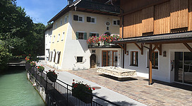 Ein charmantes Gebäude am Wasser mit Blumenkästen und einer einladenden Terrasse. Der ruhige Fluss nebenan verleiht der Szene eine idyllische Atmosphäre.
