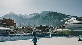 Eine Eisbahn in einer malerischen Berglandschaft. Kinder fahren im Schnee und genießen den Wintertag.