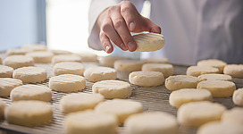 Eine Hand legt einen Keks auf ein Gestell mit vielen weiteren Keksen. Die Kekse sind hell und frisch gebacken.