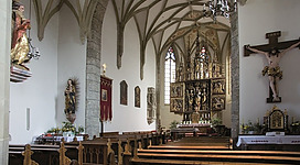 Flügelaltar Gampern in Gampern: Das Bild zeigt ein imposantes historisches Gebäude mit hohen Gewölbedecken und reich verzierten Säulen. Im Inneren befindet sich ein prunkvoll ausgestatteter Altar mit kunstvollen Schnitzereien und Statuen.