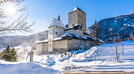 Eine alte Burg in schneebedeckter Landschaft. Der Himmel ist klar und die Sonne strahlt.