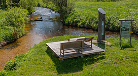 Ein Rastplatz bei der Zwischenstromwiese in Weitersfelden auf einer Wiese mit einer großen Holzliege. Rechts und links neben dem Rastplatz fließen die Schwarze und Weiße Aist zur Waldaist zusammen.